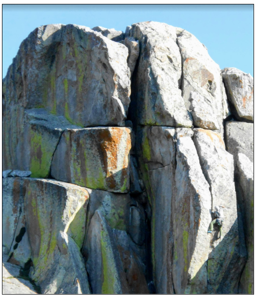 A detailed view of a massive granite boulder split by a deep vertical crack under a clear blue sky.