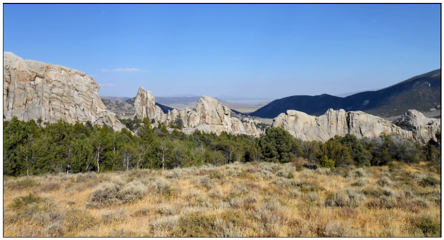 A wide panoramic landscape of towering granite spires and rock formations rising out of a desert valley in Idaho.