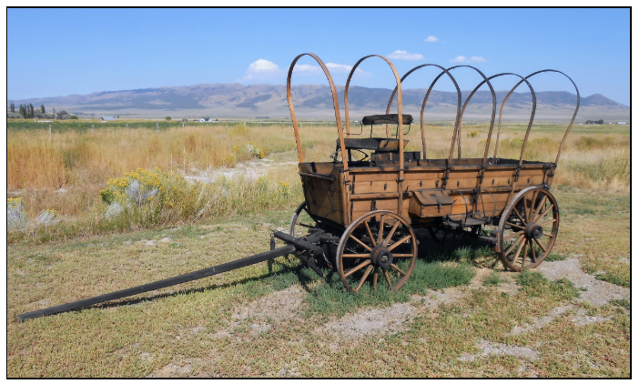 A historic wooden covered wagon frame sitting on a grassy field to mark the original California Trail route.