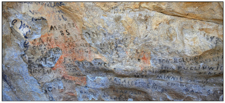 Historic pioneer signatures and dates written in dark axle grease across a weathered granite rock face.