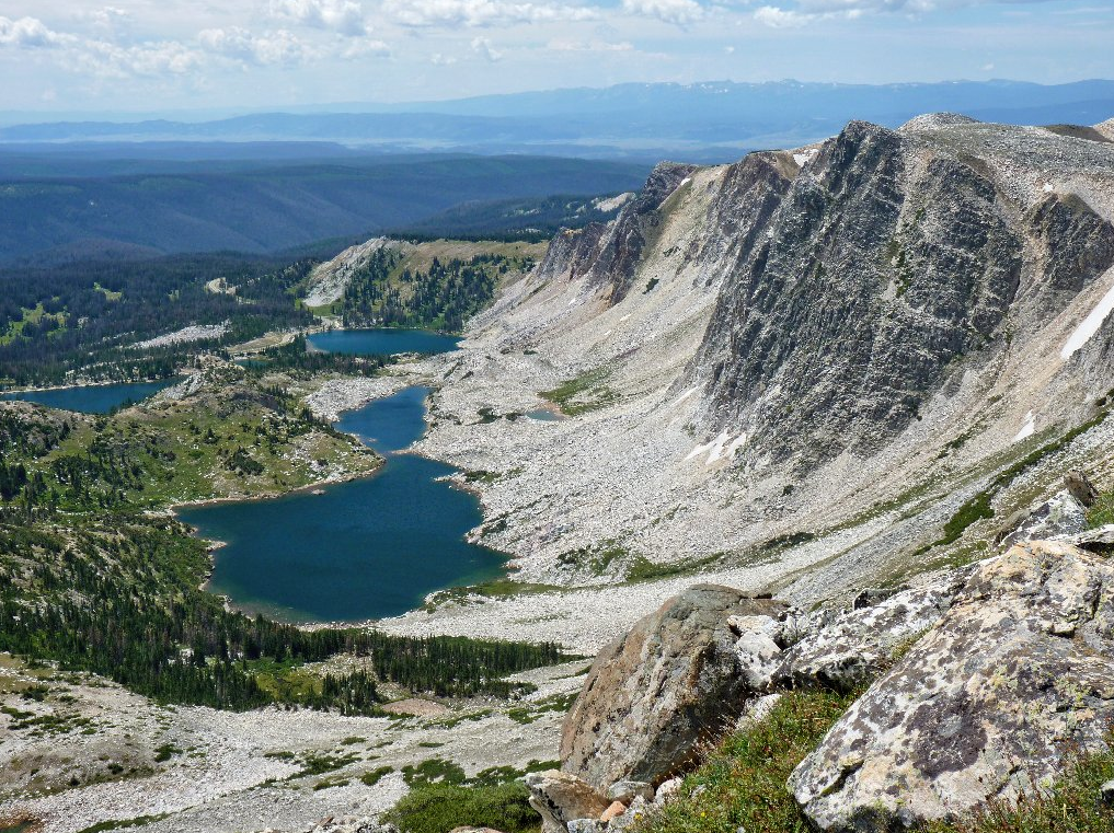 High-altitude aerial view looking down at the deep blue alpine glacial lakes cradled below the quartzite cliffs of Medicine Bow Peak, Wyoming.