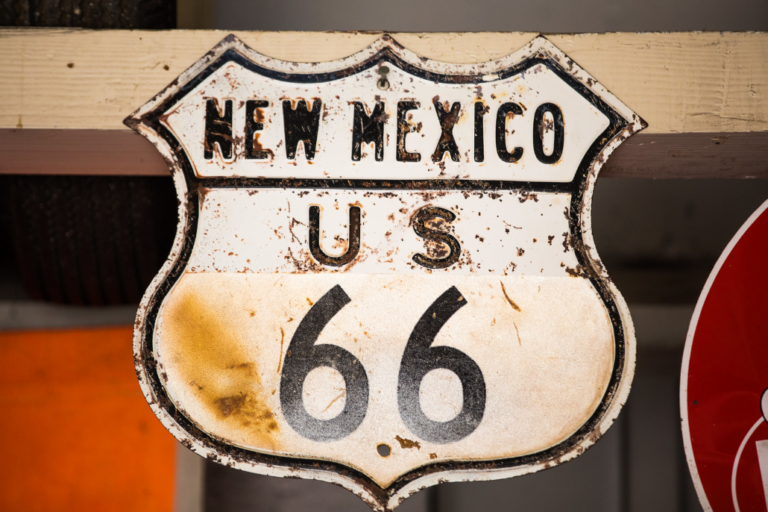 A weathered and rusty metal shield sign for New Mexico US highway 66 hanging indoors.