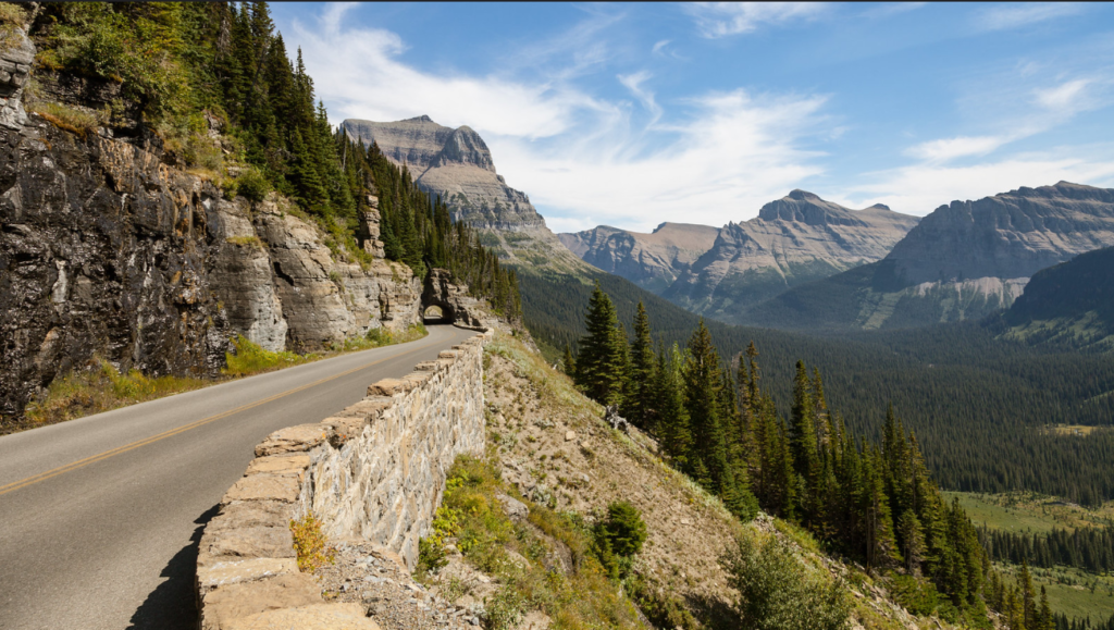 A paved section of the Going-to-the-Sun Road winding past a stone retaining wall.