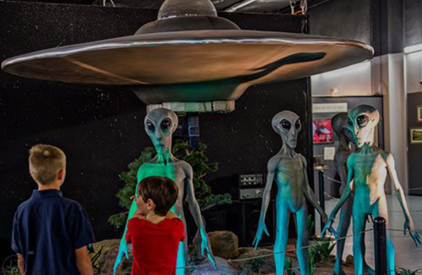 Interior view of the Roswll UFO Museum showing colorful paintings of flying saucers and sulptures of their alien pilots.