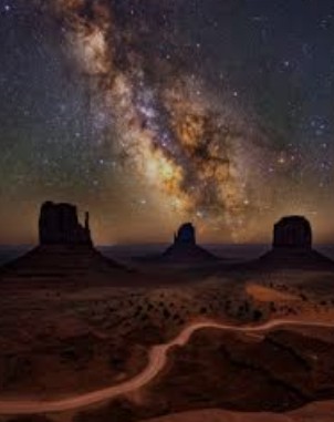 Milky Way galaxy arching over Monument Valley buttes at night with a winding road