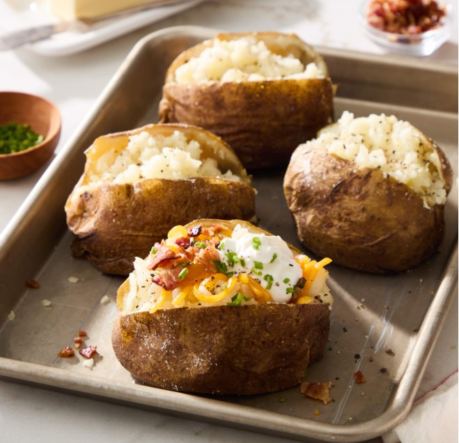 Loaded baked Idaho potatoes with cheese, bacon, sour cream, and chives on a baking tray