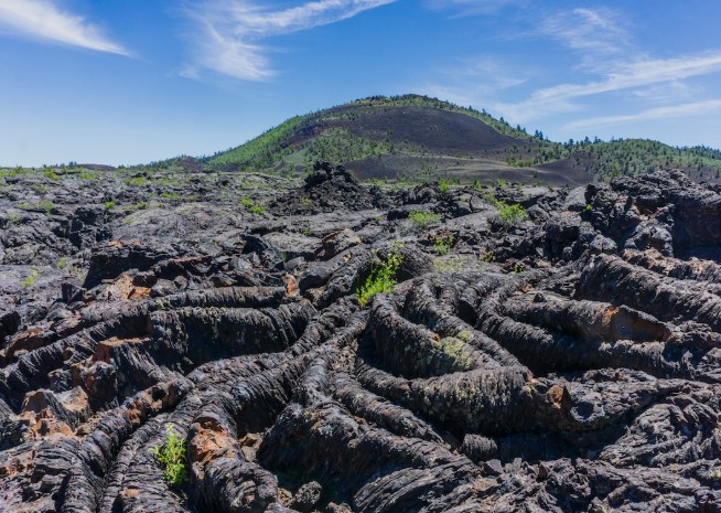 A close-up of textured black volcanic rock and ropy pahoehoe lava flows under a blue sky at Craters of the Moon in Idaho.