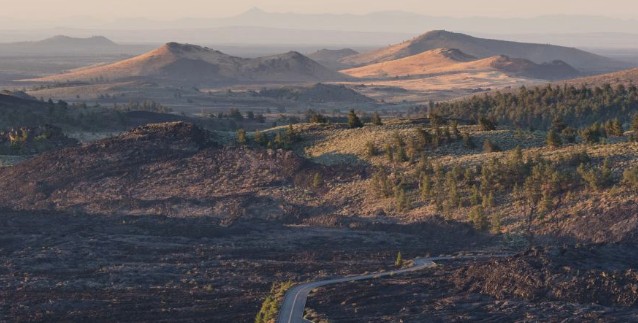 Wide-angle view of volcanic cinder cones and scattered vegetation at Craters of the Moon National Monument during the golden hour.