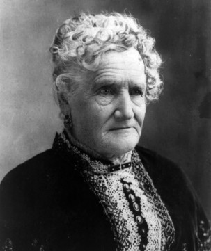 Black and white close up studio portrait of an elderly Esther Hobart Morris with curly white hair wearing a lace collar dress