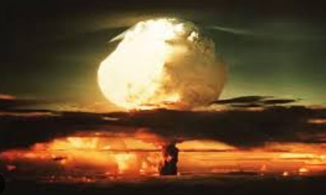 Vintage color photograph of a bright atomic bomb mushroom cloud explosion lighting up the sky over the Nevada desert horizon.