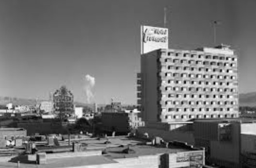 Black and white historic photograph from 1957 showing an atomic bomb test mushroom cloud visible from a Las Vegas hotel rooftop.