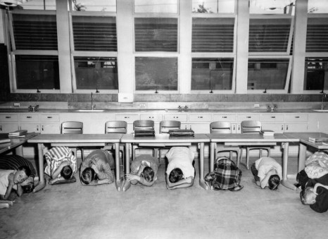 Historical photograph placeholder representing a 1960s classroom A-bomb drill with school children practicing duck and cover techniques.