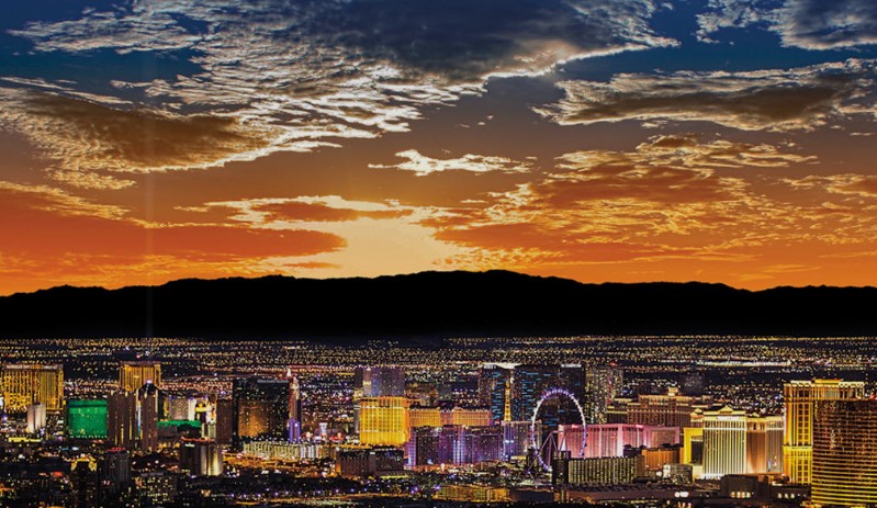 Panoramic vibrant view of the illuminated Las Vegas Strip skyline and mountains at sunset.