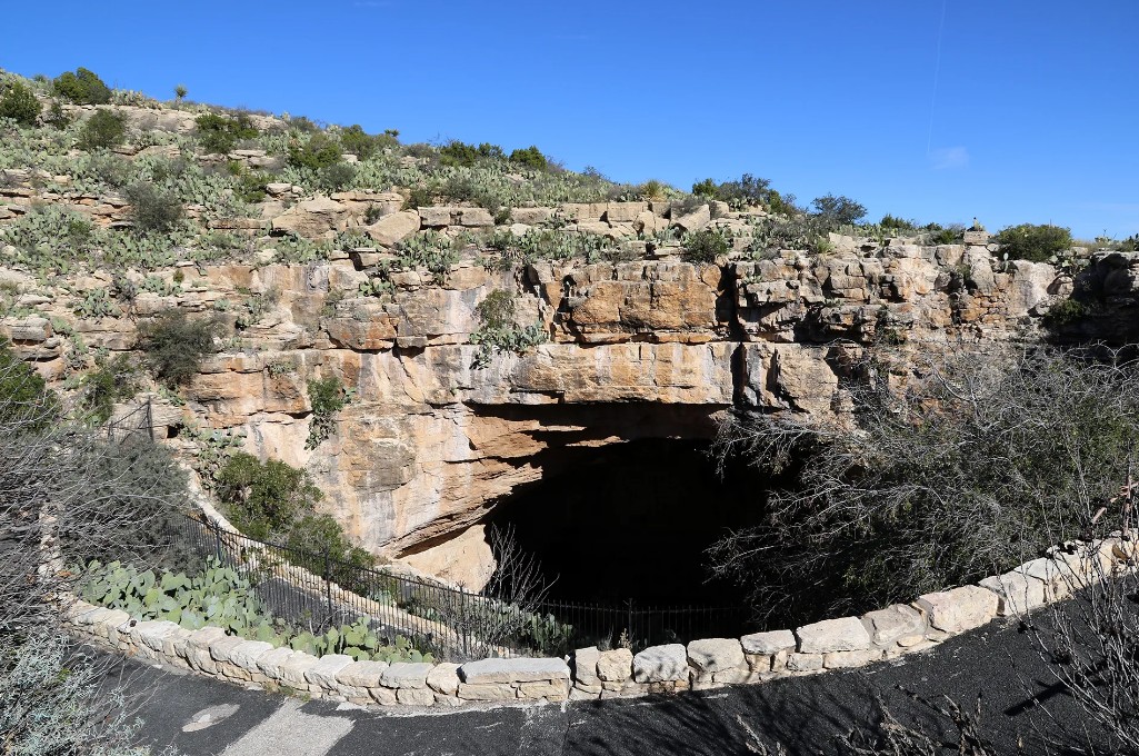 A wide view of the rocky desert hillside surrounding the large natural limestone opening of Carlsbad Caverns.