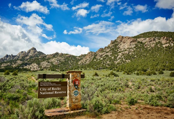 A stone entrance sign for the City of Rocks Idaho National Reserve beneath scenic desert mountains.
