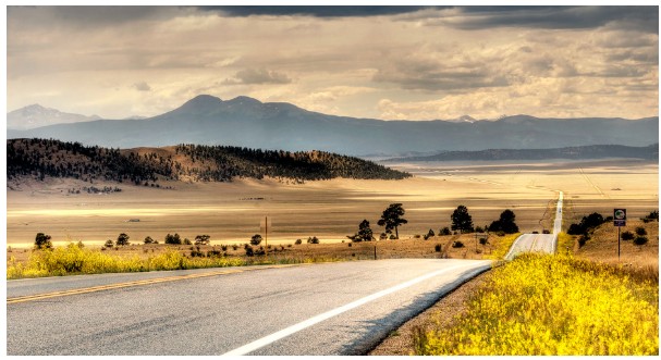 Modern paved highway stretching toward a vast valley and distant mountains at sunset.