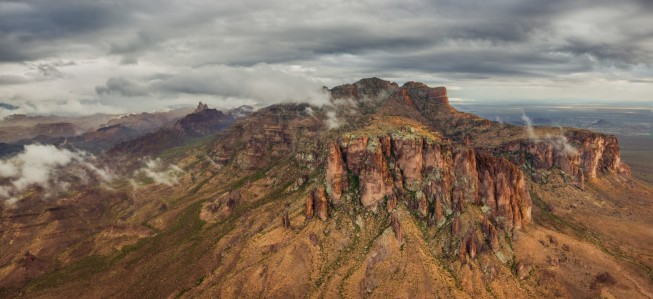 Atmospheric high-altitude/aerial shot looking down across rugged volcanic mountain ridges with scattered clouds.