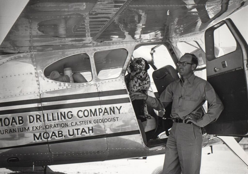 Black and white photo from the 1960s of Charlie Steen, his plane, and his dog, Butch.