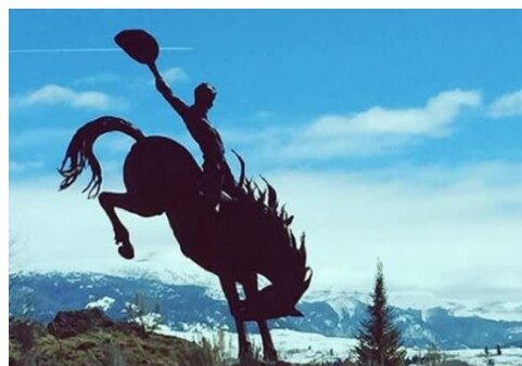 Silhouette of cowboy riding bucking horse against blue sky with white clouds